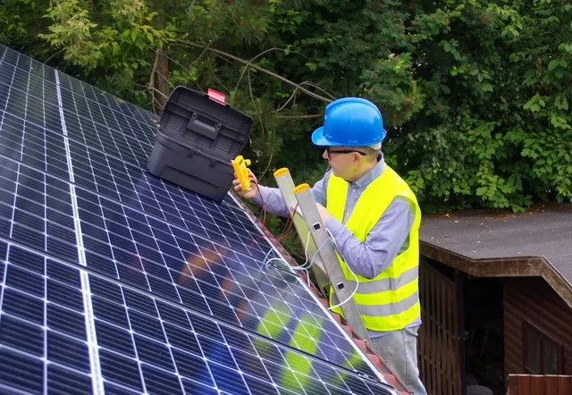 Worker in safety gear and hard hat setting up home solar panels.