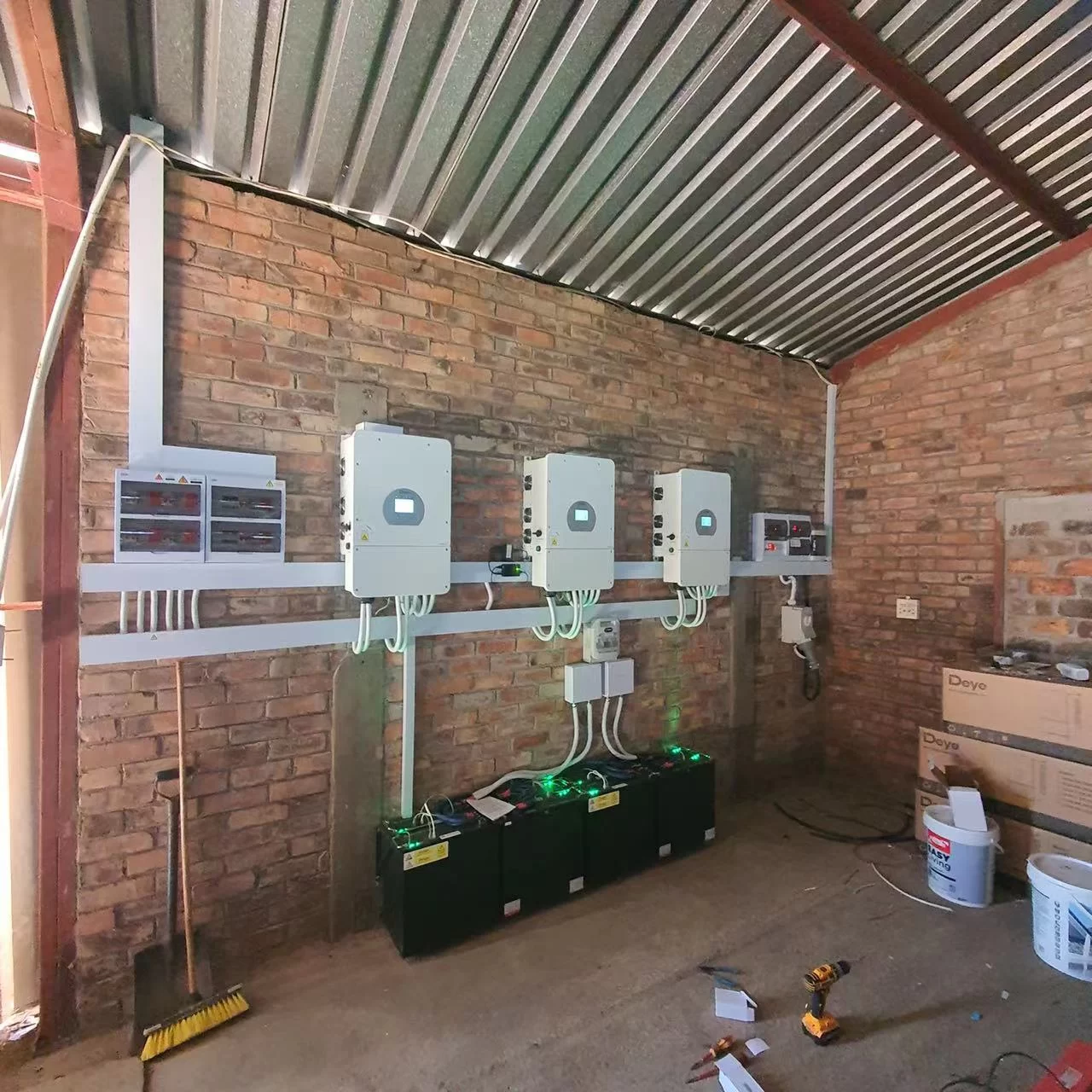 A room with three solar panels on the roof and a brick wall, featuring a Lithium-Ion Battery and Inverter.