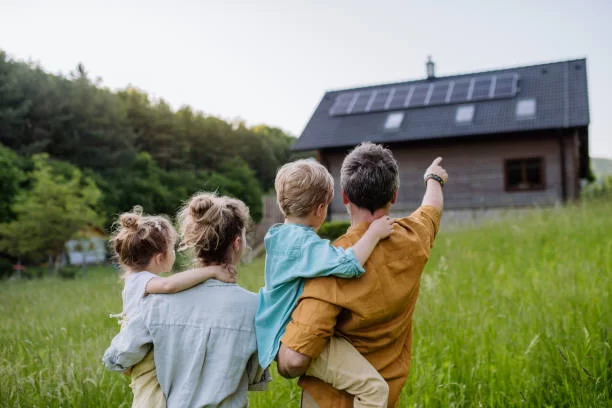 A family with children standing in front of a house with solar panels, showcasing sustainable living with solar home power systems.